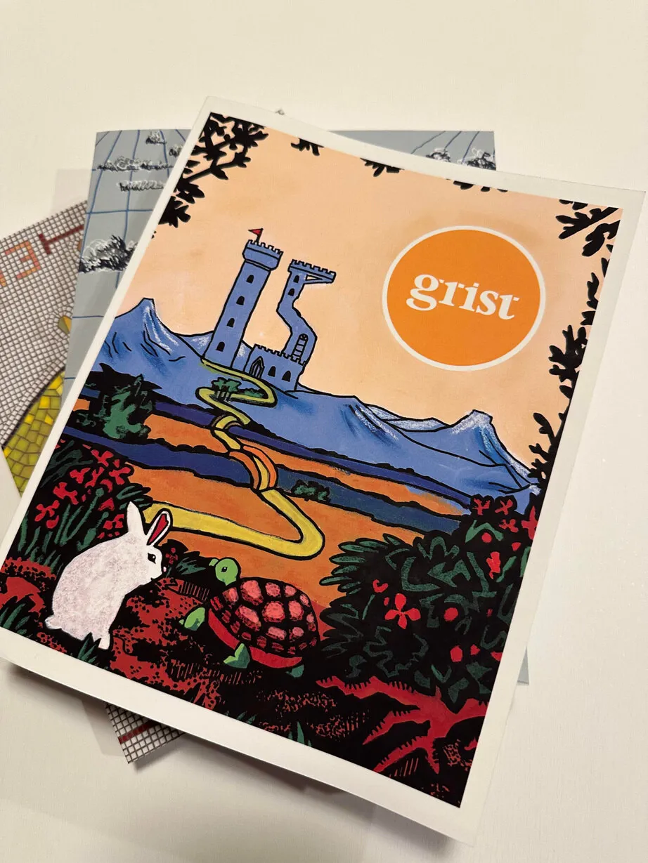 A printed copy of Grist journal, its illustrated cover resting on a stack of other journals.