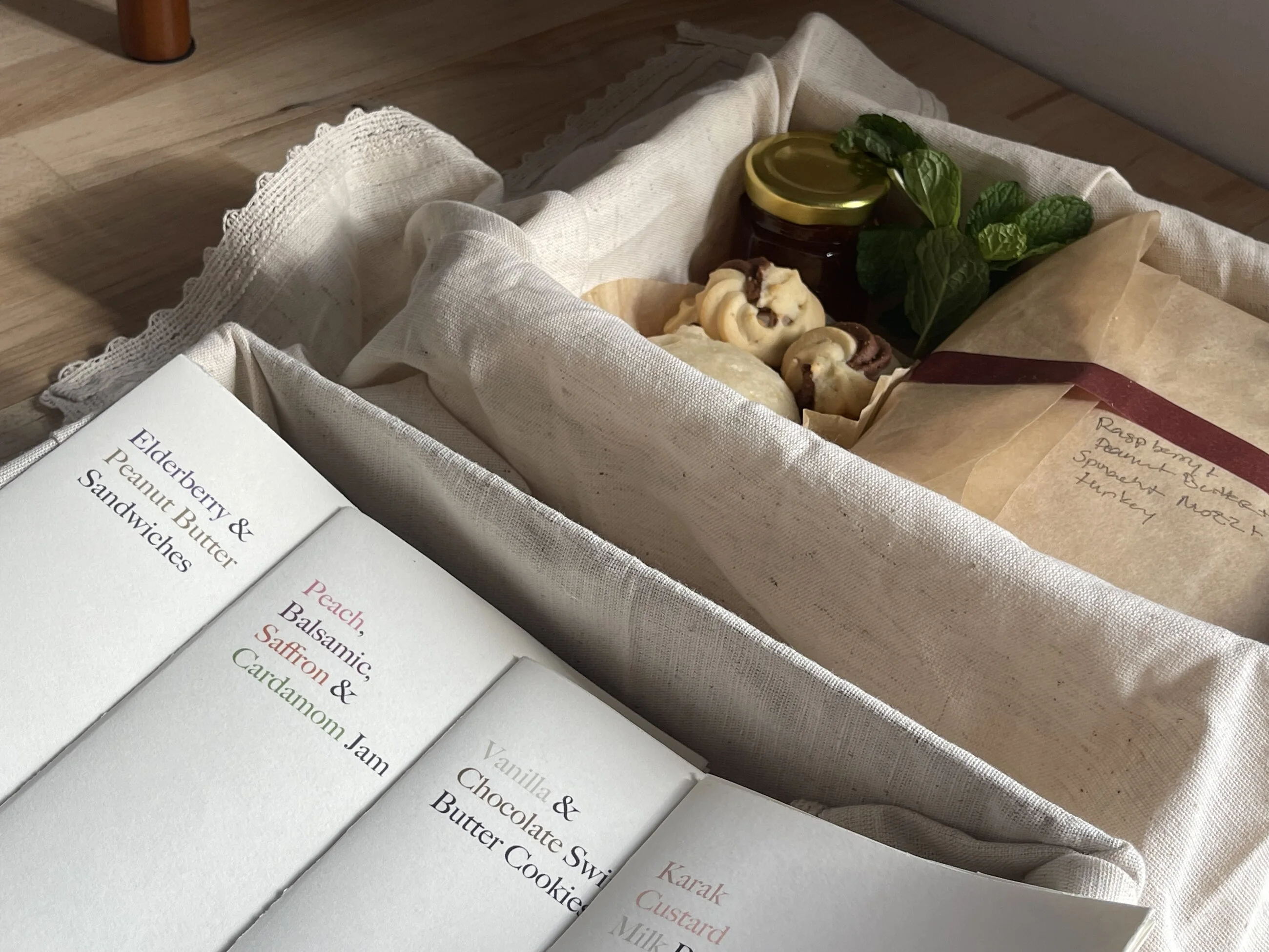 Four small recipe books fanned inside the linen box lid: Elderberry & Peanut Butter Sandwiches; Peach, Balsamic, Saffron & Cardamom Jam; Vanilla & Chocolate Swirl Butter Cookies; Karak Custard Milk Bao.