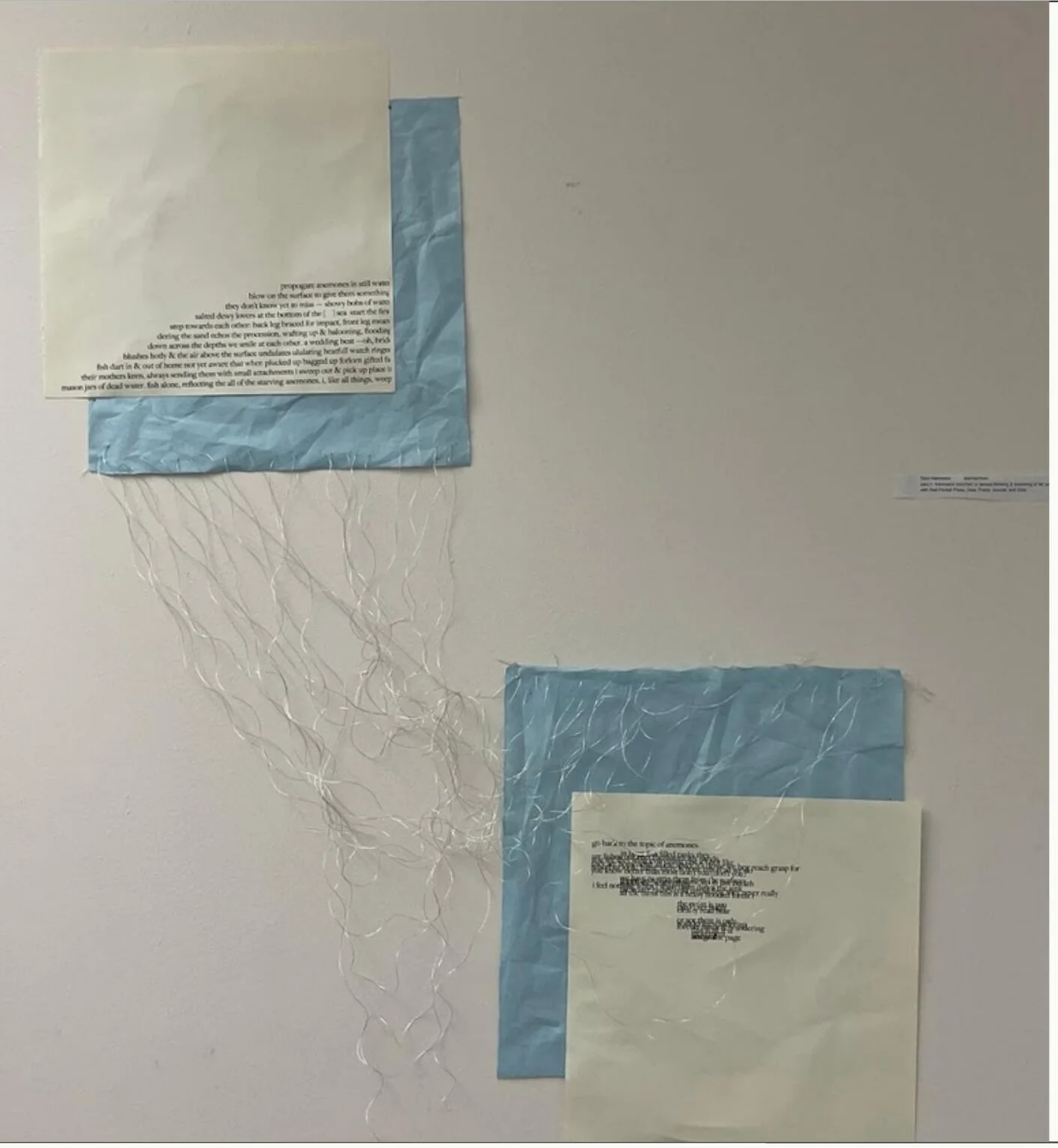 Two clusters of text printed on pale paper pinned over sheets of blue rice paper, silver threads trailing from their lower edges.