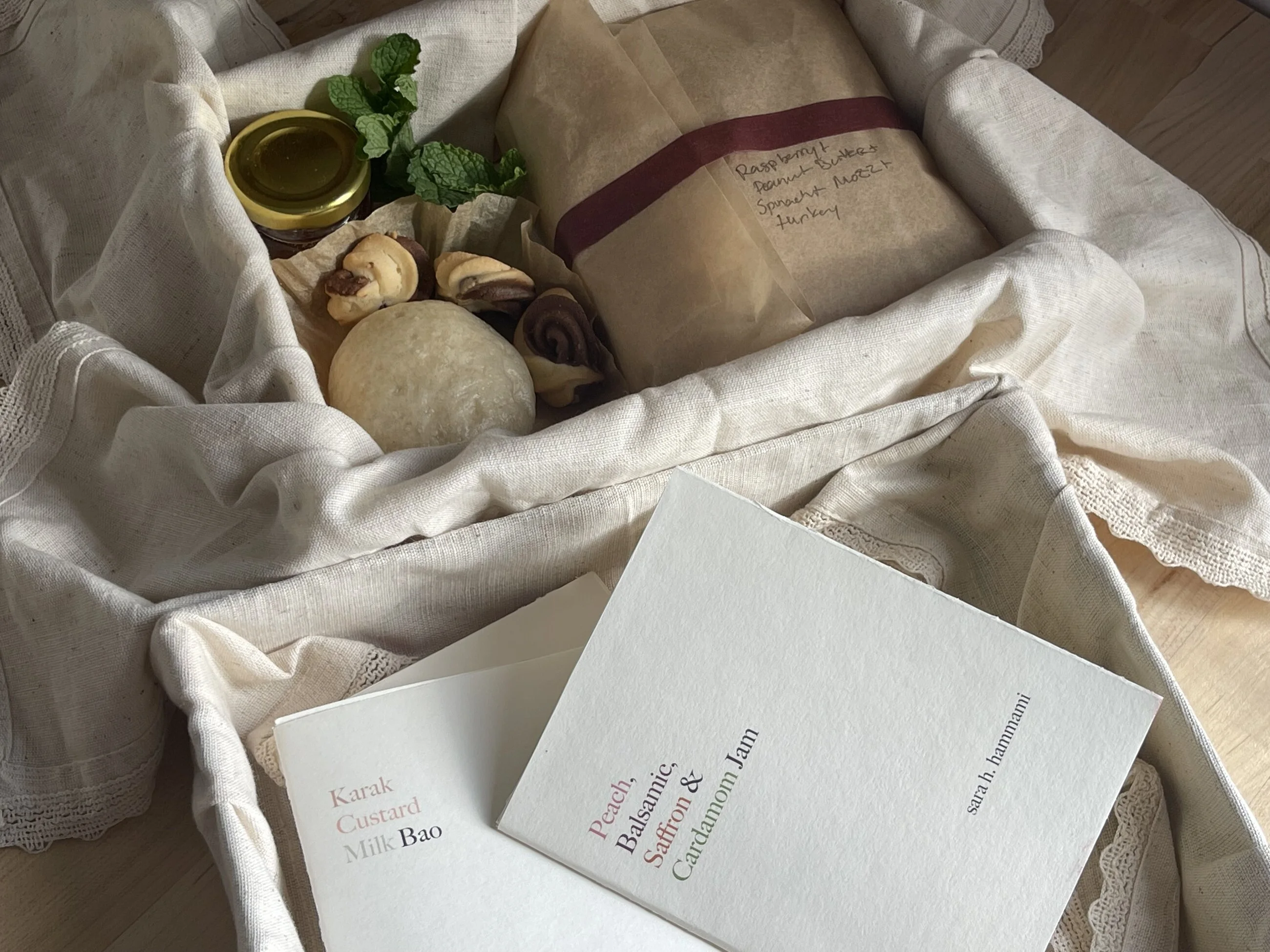 Two of the recipe books resting on the linen — Karak Custard Milk Bao, and Peach, Balsamic, Saffron & Cardamom Jam — beside the spine signed sara h. hammami.