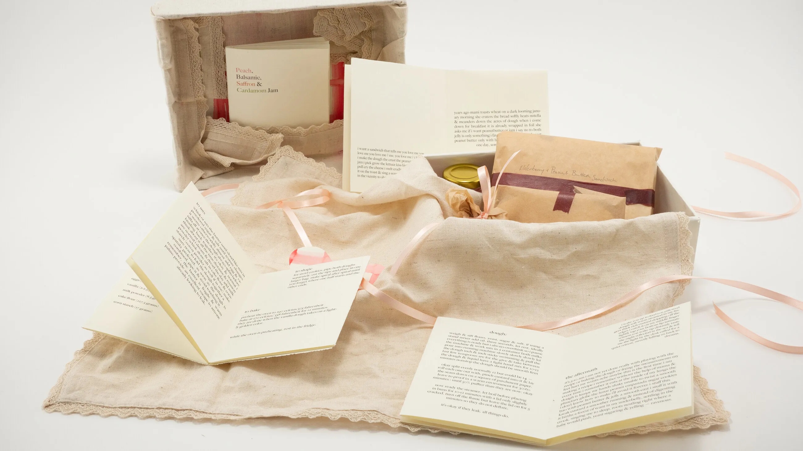 A linen-lined box opened on a table, its fold-out recipe books unfurled across a lace-edged cloth, ribbons trailing.