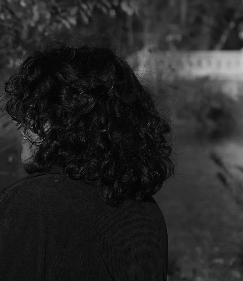 Sara, photographed from behind in black and white, dark curls against a soft riverside light.